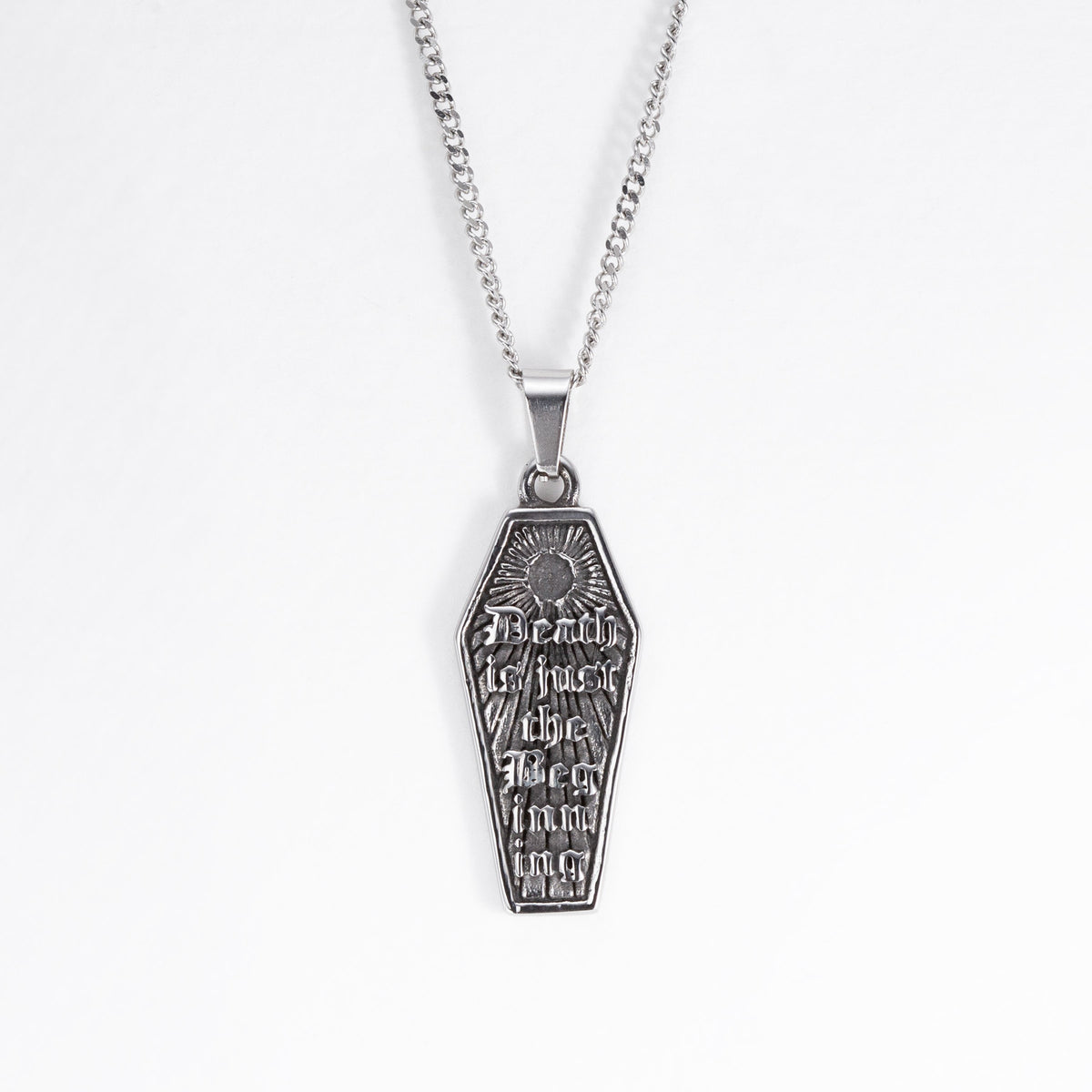 A stainless steel coffin-shaped pendant necklace with engraved gothic text and a sunburst design, hanging from a silver chain against a plain white background.