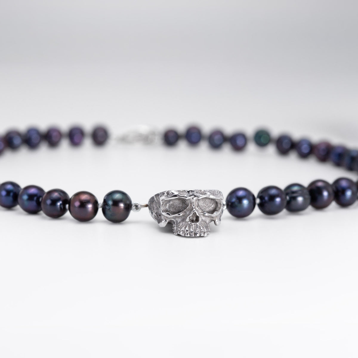 Angled front view of the Nick Von K Rebirth necklace with dark iridescent pearls and a sculpted skull pendant.