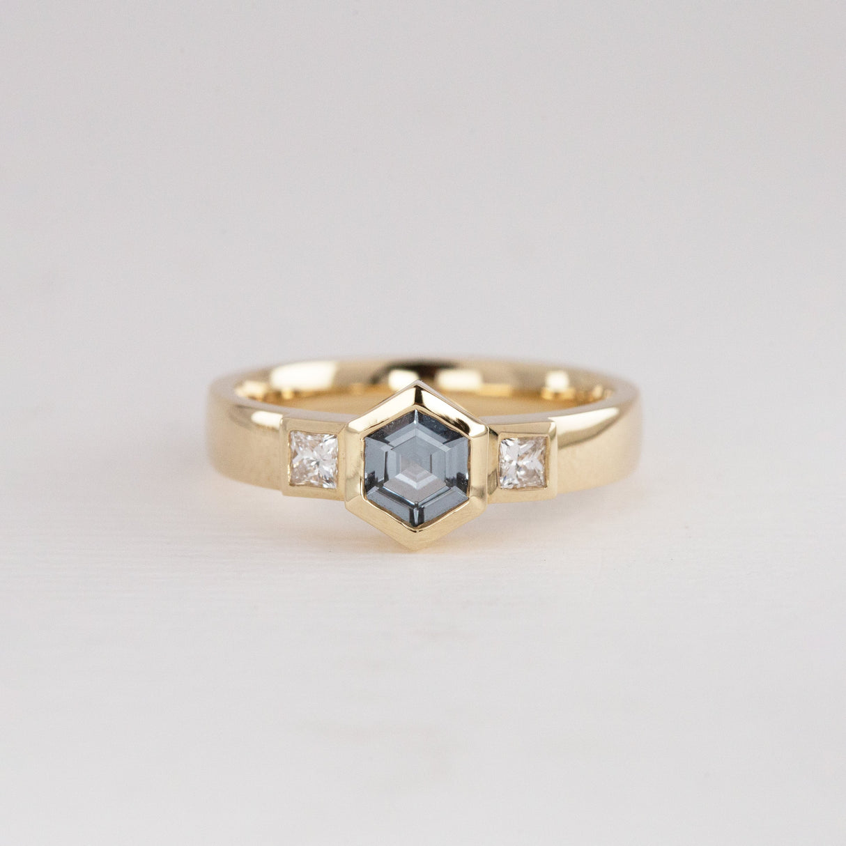 Gold ring with a central hexagonal Spinel gemstone and smaller diamonds set either side.