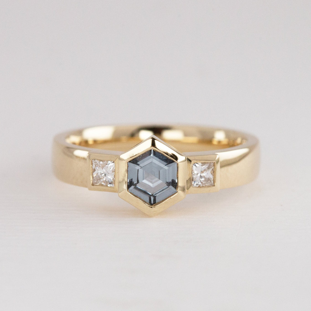 Gold ring with a central hexagonal Spinel gemstone and smaller diamonds set either side.