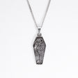 A silver coffin-shaped pendant necklace featuring an embossed skeleton figure, suspended from a silver box chain against a plain white background.