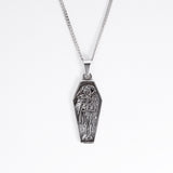 A silver coffin-shaped pendant necklace featuring an embossed skeleton figure, suspended from a silver box chain against a plain white background.