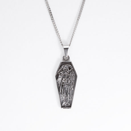 A silver coffin-shaped pendant necklace featuring an embossed skeleton figure, suspended from a silver box chain against a plain white background.