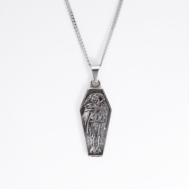 A silver coffin-shaped pendant necklace featuring an embossed skeleton figure, suspended from a silver box chain against a plain white background.