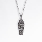 A stainless steel coffin-shaped pendant necklace with engraved gothic text and a sunburst design, hanging from a silver chain against a plain white background.