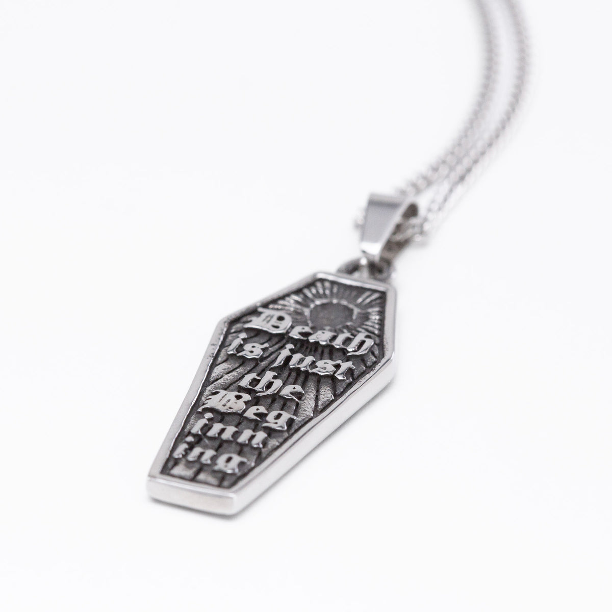 A silver coffin-shaped pendant necklace with the gothic text 'Death is just the beginning' engraved on a textured background, shown on a clean white background.