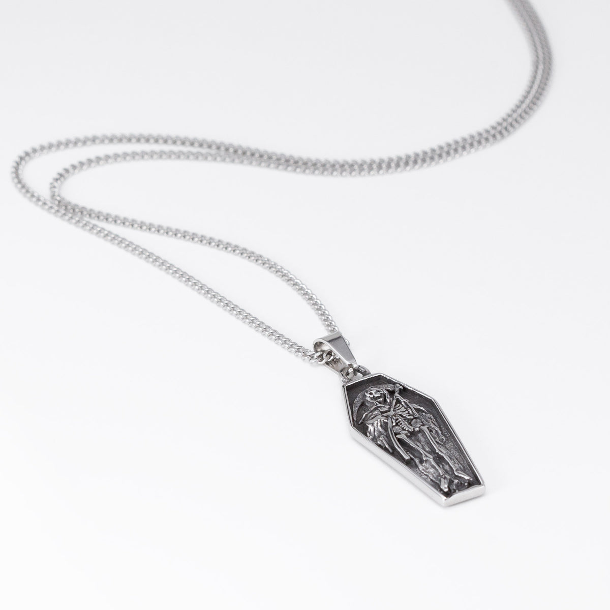 A silver coffin-shaped pendant necklace featuring an embossed grim reaper figure, displayed on a clean white background.