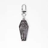 A stainless steel coffin-shaped bag charm keychain featuring an embossed skeleton reaper figure, complete with a lobster clasp at the top, shown against a plain white background.