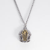A silver chain necklace with a skull-shaped pendant featuring a gold coffin inlay with a skeleton figure, set against a plain white background.