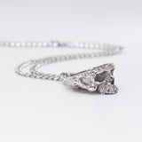 A silver chain necklace featuring a textured, organic-shaped skull pendant, photographed on a clean white background.