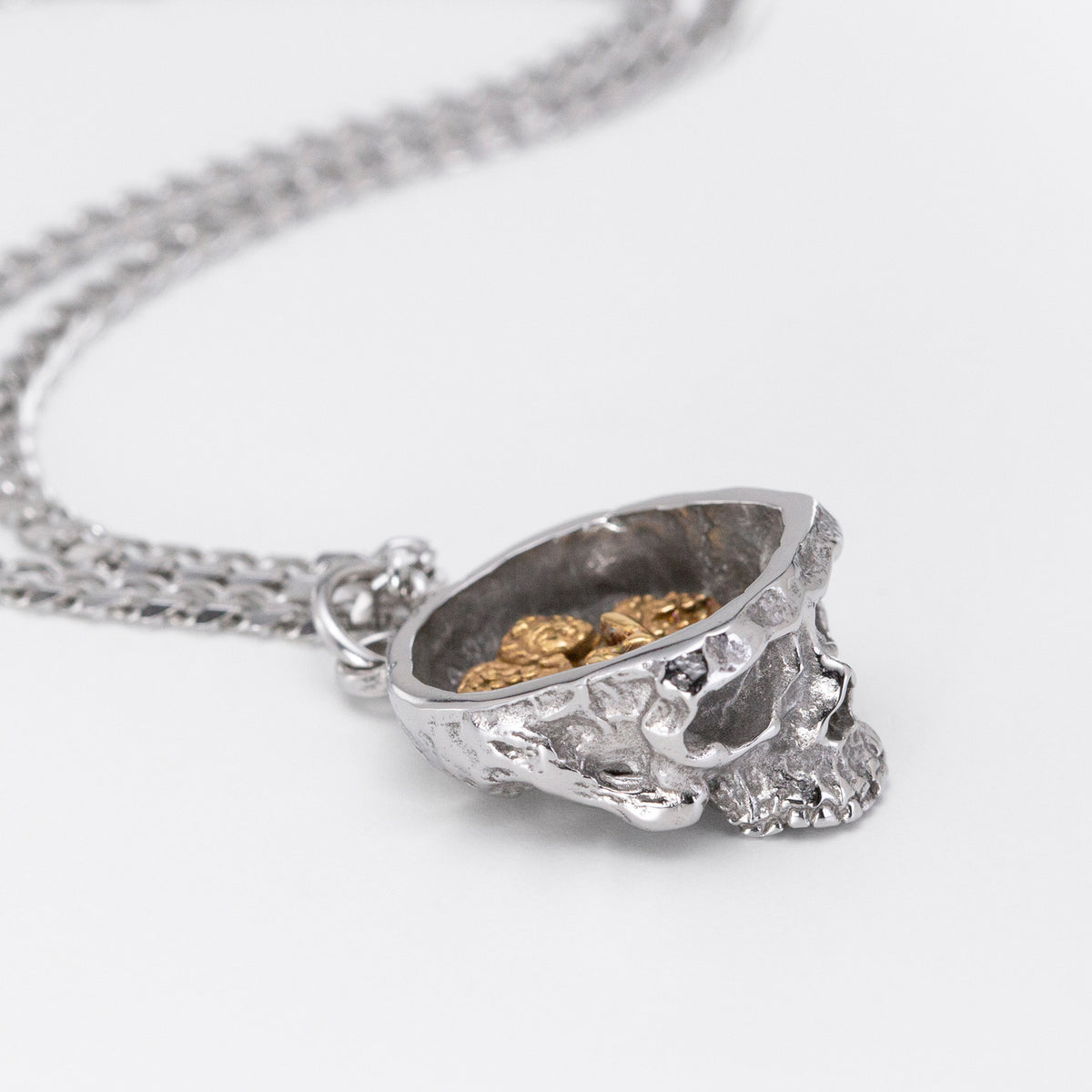 A silver-toned chain necklace with a skull-shaped pendant that opens to reveal a gold-toned interior filled with small angel-shaped charms, photographed on a clean white background.