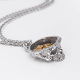 A silver-toned chain necklace with a skull-shaped pendant that opens to reveal a gold-toned interior filled with small angel-shaped charms, photographed on a clean white background.