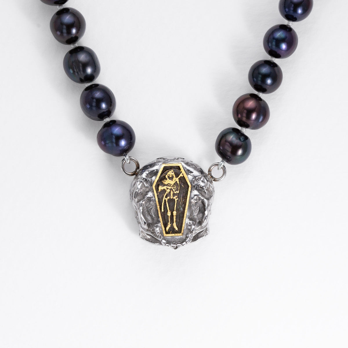 Rear detail of the Nick Von K Rebirth pearl necklace showing a gold-outlined coffin and skeletal reaper on the skull pendant.
