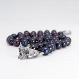 A strand of dark iridescent pearls with a silver skull pendant, photographed on a clean white background.
