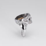 A silver skull ring with a textured, hammered finish and a polished band, photographed on a neutral light gray background.